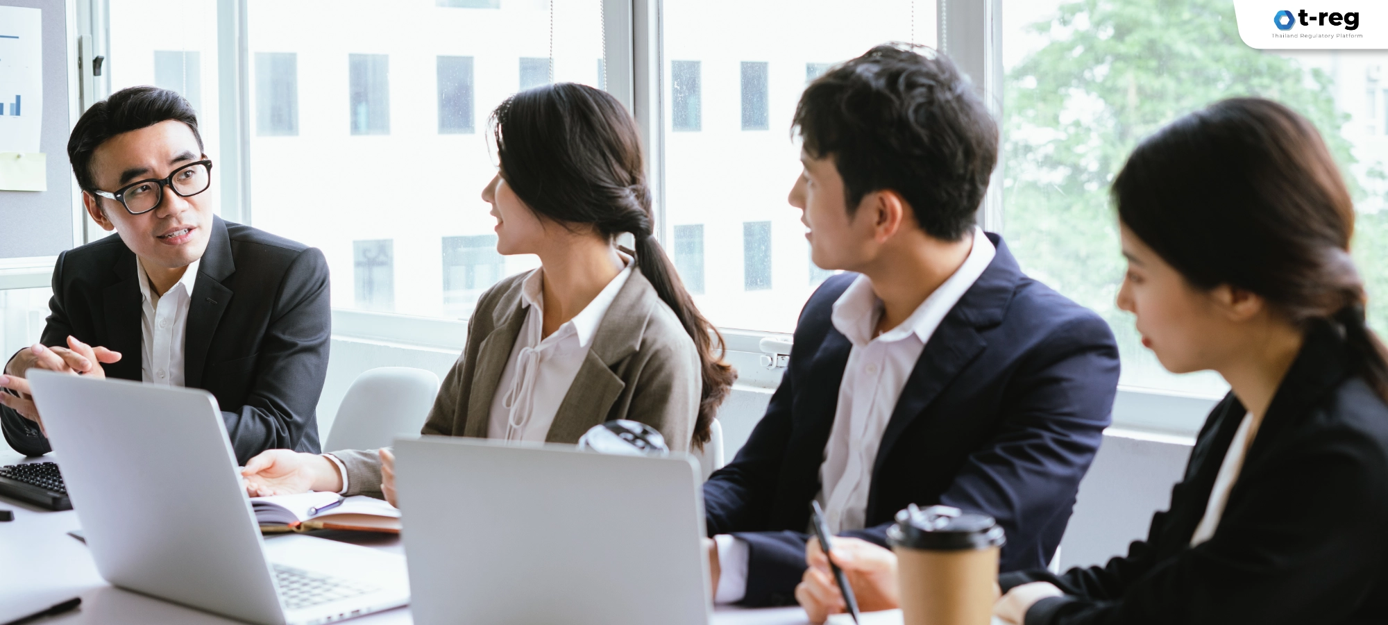 ภาพทีมงานสวมชุดสูทประชุมร่วมกันในห้องประชุม พร้อมแล็ปท็อปและเอกสาร แสดงการทำงานอย่างมืออาชีพ